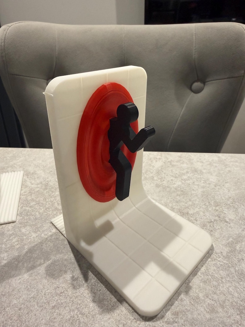 May include: A white, 3D-printed desk organizer featuring a red circular portal and a black silhouette of a person. The organizer has a rectangular base and a vertical back with a grid pattern.