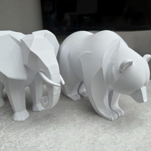 May include: Two white geometric animal sculptures: an elephant with tusks and a bear. The elephant stands on four legs, and the bear is in a walking pose. Both are made of a solid, matte material.