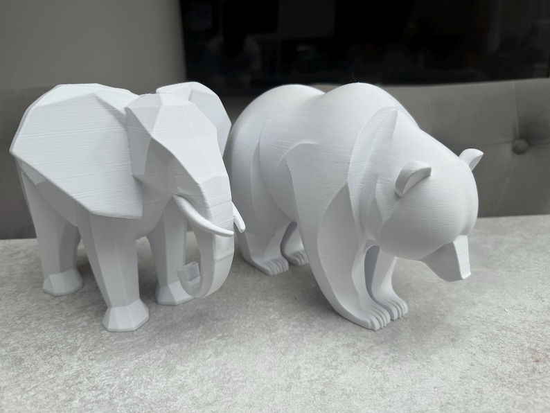 May include: Two white geometric animal sculptures: an elephant with tusks and a bear. The elephant stands on four legs, and the bear is in a walking pose. Both are made of a solid, matte material.