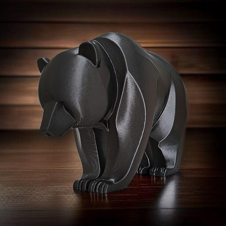 May include: A black bear figurine with a geometric design. The bear is standing on all fours, with its head slightly lowered. The figurine is made of a dark, matte material and has a modern, minimalist aesthetic.