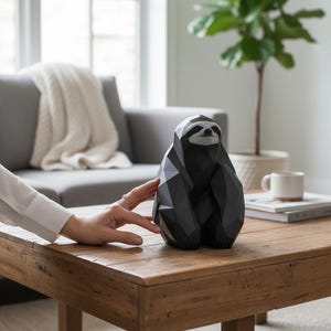 May include: A geometric, black and gray sloth sculpture sits on a wooden coffee table. The sloth has a stylized design with angular facets. The sculpture is a decorative item, adding a modern touch to home decor.