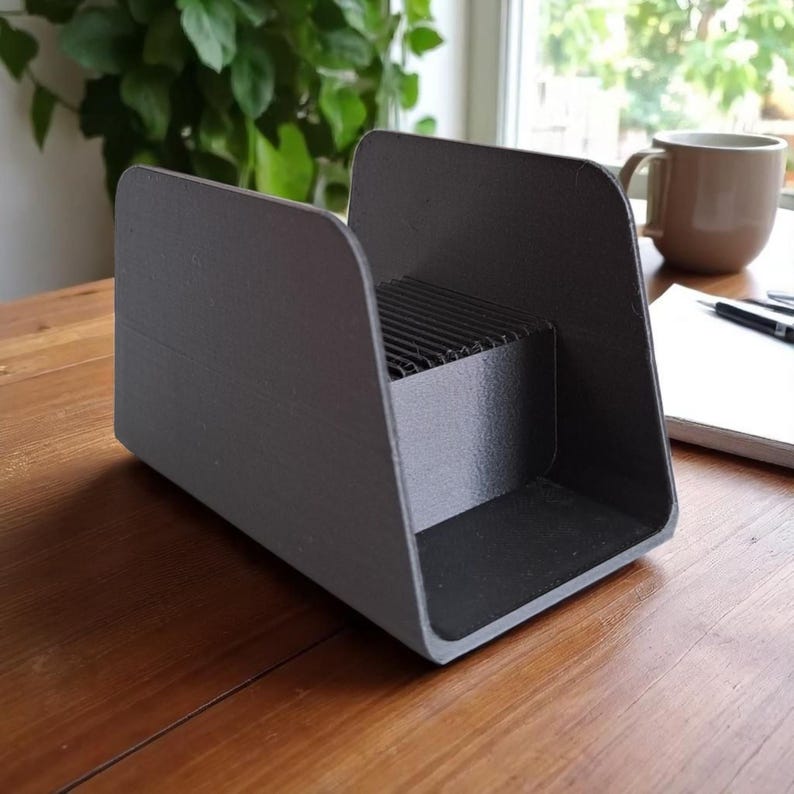 May include: A dark gray desk organizer with a rectangular base and curved sides. The organizer has a section with horizontal slats. The item is sitting on a wooden surface.