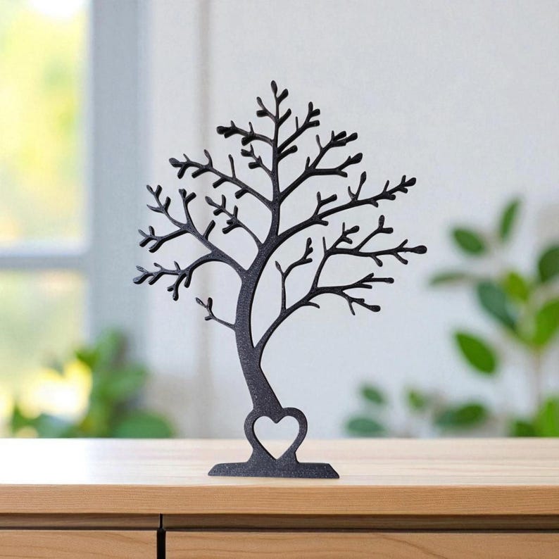 May include: A black metal tree-shaped jewelry holder with a heart cutout at the base. The tree has many branches for hanging necklaces and other jewelry. The holder is displayed on a wooden surface.