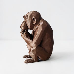 May include: A brown geometric sculpture of a chimpanzee in a seated position, with its hands clasped near its face. The sculpture has a faceted design, giving it a modern, angular appearance. The primate figurine is a decorative item.