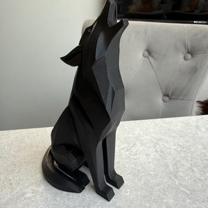 May include: A black geometric wolf sculpture in a howling pose. The artwork is made of solid material and has a modern, angular design. The wolf is sitting on a light-colored surface.