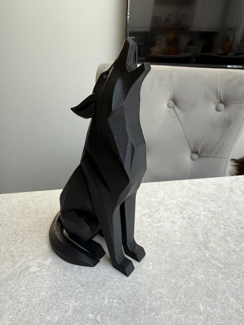 May include: A black geometric wolf sculpture in a howling pose. The artwork is made of solid material and has a modern, angular design. The wolf is sitting on a light-colored surface.