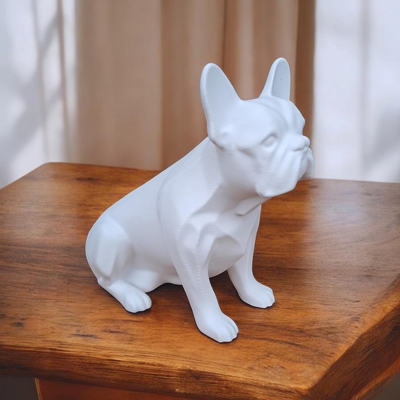 May include: White ceramic figurine of a French bulldog sitting with its head turned to the side. The figurine is detailed with a textured surface and realistic features.