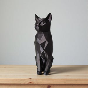 May include: A black geometric cat sculpture with a faceted design. The cat is sitting upright on a wooden surface, with its ears perked up and its gaze directed to the left. The sculpture has a modern, minimalist aesthetic.
