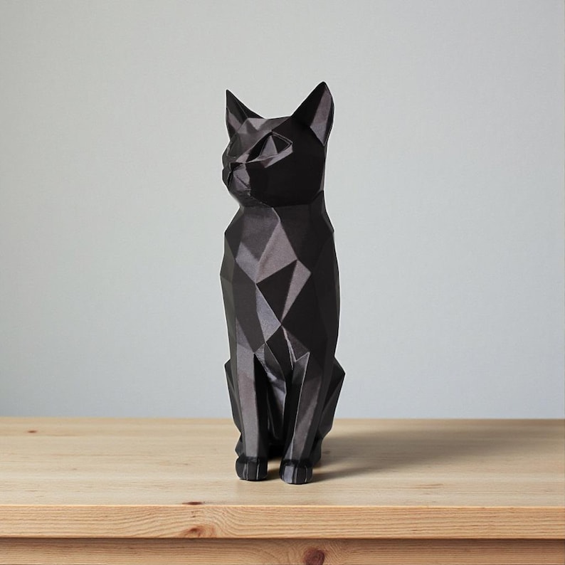 May include: A black geometric cat sculpture with a faceted design. The cat is sitting upright on a wooden surface, with its ears perked up and its gaze directed to the left. The sculpture has a modern, minimalist aesthetic.