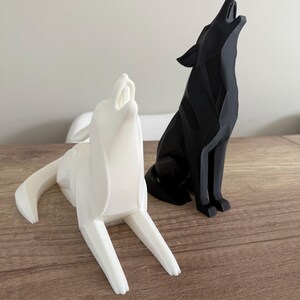 May include: Two geometric wolf sculptures. One is white and the other is black. Both are in a howling pose, with their heads tilted back and mouths open. The sculptures are placed on a wooden surface.
