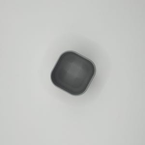 May include: A small, square, gray container with rounded corners. The container is empty and appears to be made of a solid material. The interior is a darker shade of gray than the exterior. The container is set against a white background.