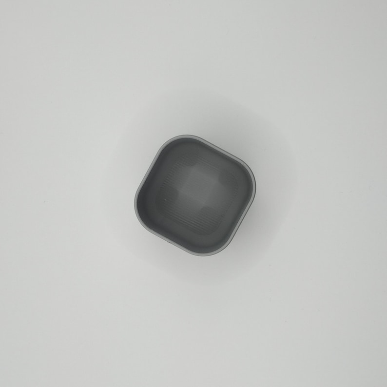 May include: A small, square, gray container with rounded corners. The container is empty and appears to be made of a solid material. The interior is a darker shade of gray than the exterior. The container is set against a white background.