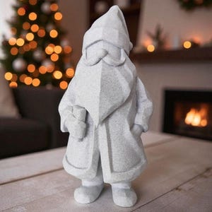 K&ouml;nnte beinhalten: Eine hellgraue, geometrische Zwergenstatue mit langem Mantel, Bart und spitzer M&uuml;tze. Die Statue hat die H&auml;nde in den Taschen und steht auf einer Holzoberfl&auml;che. Im Hintergrund ist ein Weihnachtsbaum zu sehen.