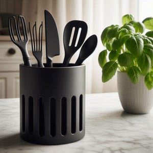 May include: A black utensil holder with a slotted design, containing a whisk, fork, knife, slotted spoon, and solid spoon. A potted basil plant is to the right on a marble countertop. The utensils and holder are all black.