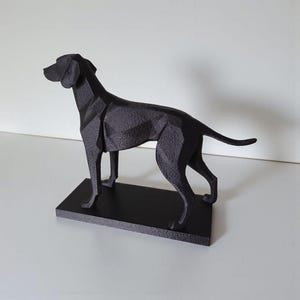 May include: A black geometric dog sculpture on a rectangular base. The sculpture has a modern, angular design with a matte finish. The dog is depicted in a standing pose, with its head raised and tail slightly curved. The sculpture is made of a solid material.