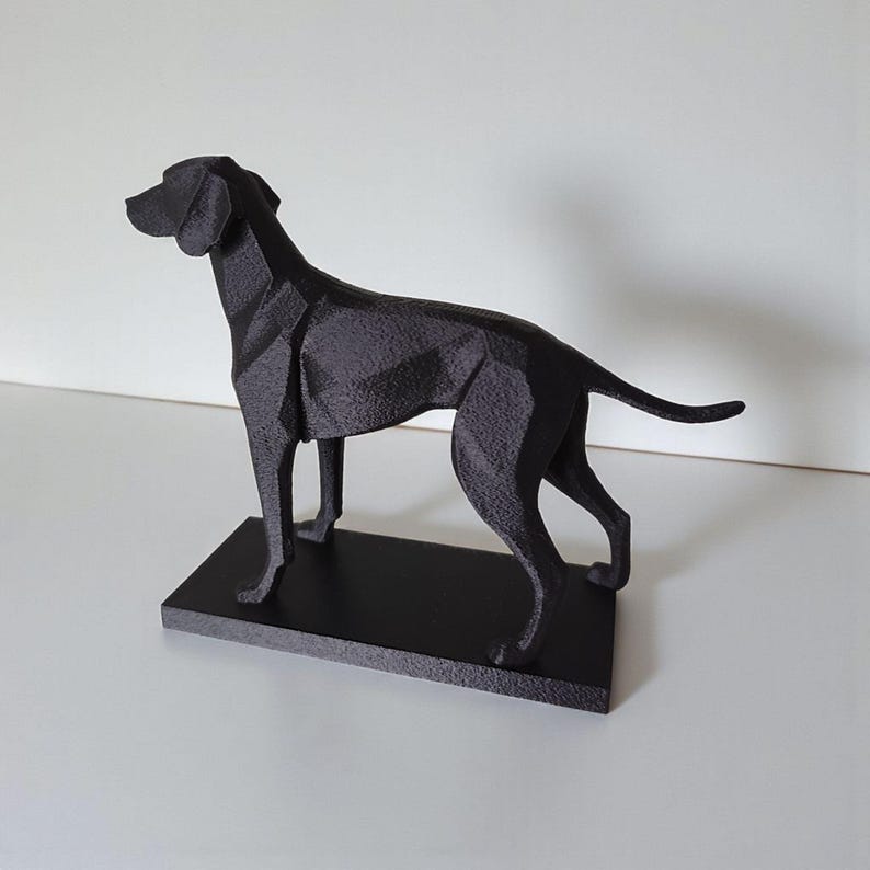 May include: A black geometric dog sculpture on a rectangular base. The sculpture has a modern, angular design with a matte finish. The dog is depicted in a standing pose, with its head raised and tail slightly curved. The sculpture is made of a solid material.