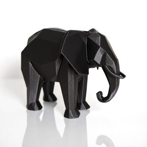 Op de afbeelding: Een zwarte geometrische olifant sculptuur met een facetontwerp. De olifant heeft grote oren, een slurf en vier poten. De sculptuur is gemaakt van een stevig materiaal en staat op een witte ondergrond.