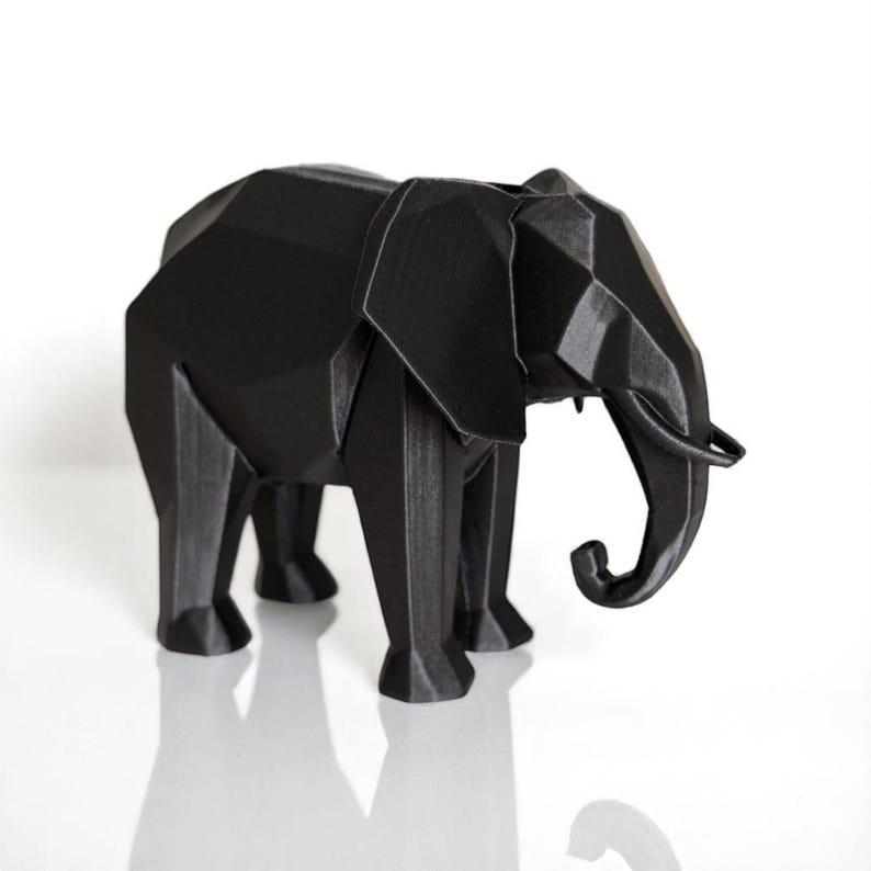 Op de afbeelding: Een zwarte geometrische olifant sculptuur met een facetontwerp. De olifant heeft grote oren, een slurf en vier poten. De sculptuur is gemaakt van een stevig materiaal en staat op een witte ondergrond.