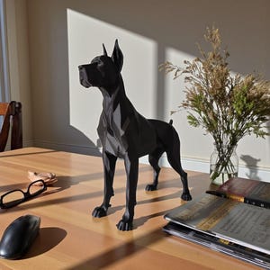 Puede incluir: Una estatua de perro negro de estilo geom&eacute;trico se encuentra sobre una mesa de madera. El perro tiene orejas puntiagudas y una constituci&oacute;n esbelta. La estatua est&aacute; junto a un jarr&oacute;n con flores secas, unas gafas y un rat&oacute;n de ordenador.