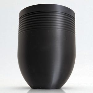 May include: A black, cylindrical object with a rounded base. The upper portion features a series of horizontal, ridged lines. The object has a smooth, matte finish and is set against a white background.