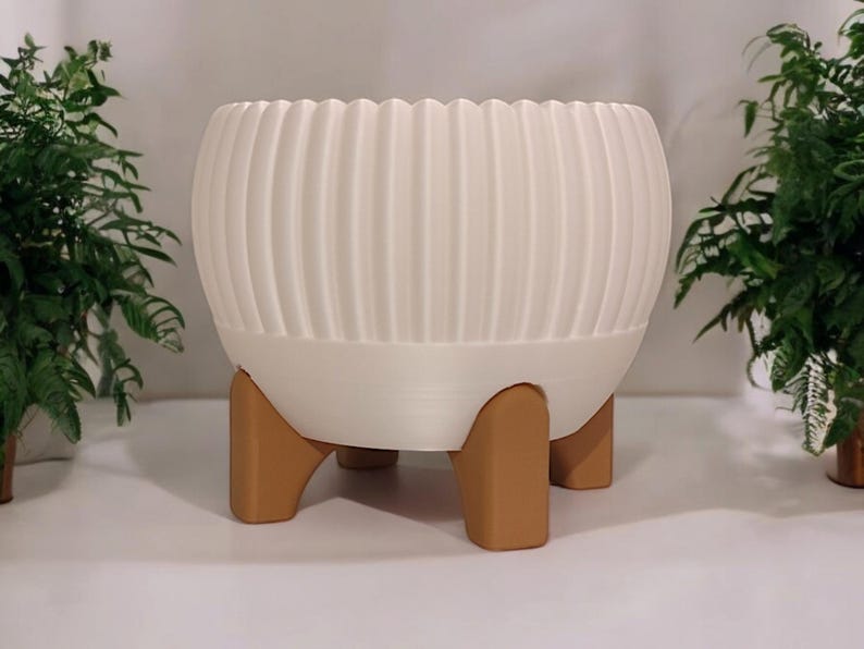 Pode incluir: Um vaso branco e canelado com formato arredondado, sustentado por tr&ecirc;s pernas castanhas. O vaso tem um design moderno e &eacute; adequado para uso interno ou externo. O vaso tem cerca de 30 cm de di&acirc;metro e 25 cm de altura.