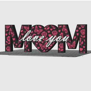 May include: A decorative MOM sign with a heart-shaped O. The letters are black with pink butterfly and rose cutouts. The heart has a pink butterfly and rose pattern with the words "love you" in white script.