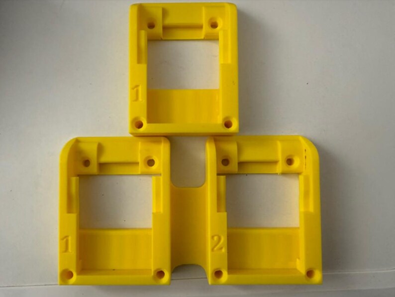 May include: Three bright yellow plastic rectangular frames with rounded corners. Each frame has a central opening and several small holes. Numbers 1 and 2 are printed on the frames.