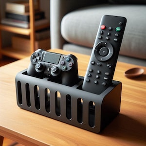 May include: A dark grey media organiser holding a black remote control and a black games controller. The organiser has a rectangular shape with vertical slots. The items are on a wooden surface.
