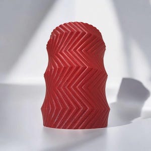 May include: A red, decorative object with a zigzag pattern. The object has a rounded top and a textured surface. The design is a series of angled lines that create a geometric pattern. The object is likely a candle or a decorative piece.