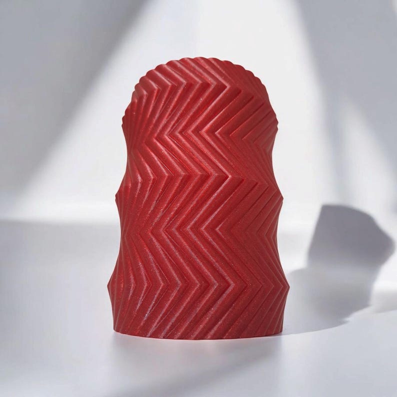 May include: A red, decorative object with a zigzag pattern. The object has a rounded top and a textured surface. The design is a series of angled lines that create a geometric pattern. The object is likely a candle or a decorative piece.