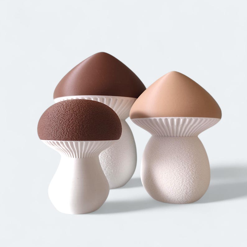 May include: Three decorative mushroom figurines. The caps are brown and tan, with textured and smooth surfaces. The stems are white with a textured finish. The mushrooms vary in size and shape, creating a whimsical display.