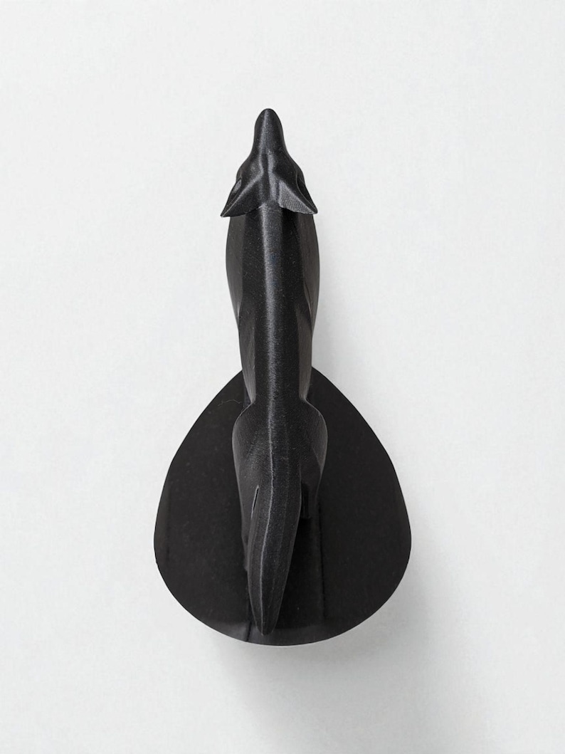 May include: A black decorative wall sculpture in the shape of a stylized animal, possibly a wolf or dog, viewed from above. The sculpture has a sleek, modern design and is mounted on a teardrop-shaped base. The artwork is made of a matte black material.