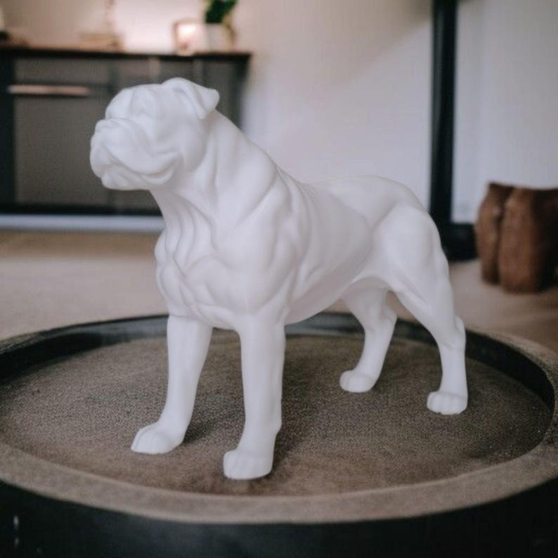 May include: A white bulldog statue, standing on a round, dark-colored surface. The sculpture is detailed, showing the dog's wrinkles and muscular build. The statue is a decorative item, likely for home decor.