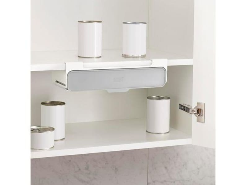 May include: A white cabinet interior with a pull-out storage shelf and several white cans. The shelf is gray and white, designed to hold items. The cabinet door is open, revealing the contents.