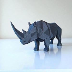 May include: A black geometric rhino sculpture with a textured surface. The rhino is standing on a white surface and has a large horn. The sculpture is a modern, minimalist design.