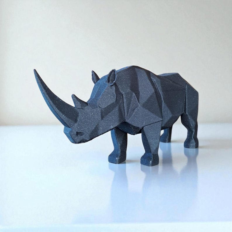 May include: A black geometric rhino sculpture with a textured surface. The rhino is standing on a white surface and has a large horn. The sculpture is a modern, minimalist design.