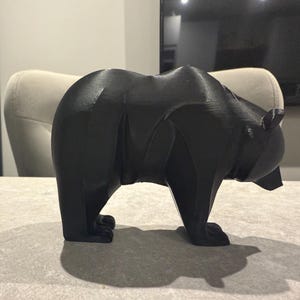 May include: A black bear figurine with a geometric design. The bear is standing on all fours, with a detailed form. The sculpture is made of a solid, dark material and is a decorative item.