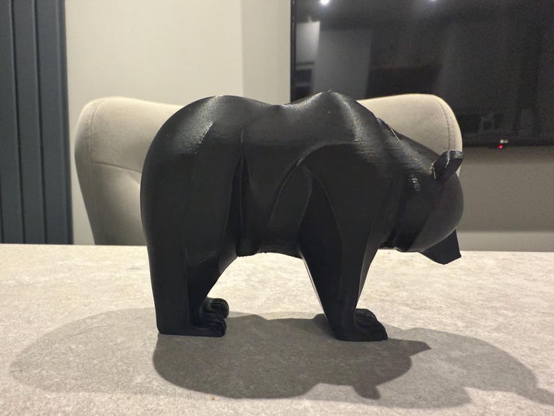 May include: A black bear figurine with a geometric design. The bear is standing on all fours, with a detailed form. The sculpture is made of a solid, dark material and is a decorative item.