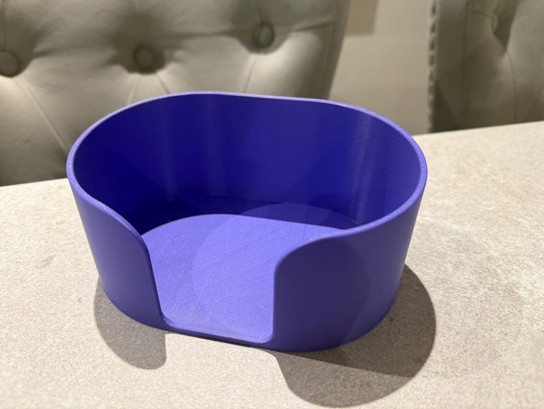 May include: A solid purple, oval-shaped container with rounded sides and a flat base. The container has a smooth, matte finish and is designed to hold small items. The object is sitting on a light-colored surface.