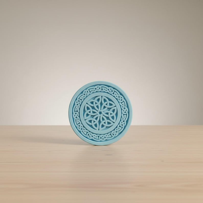 May include: A round, light blue coaster with a Celtic knot design. The coaster features a central knot pattern surrounded by a circular border of interwoven knots. The coaster is made of a solid material and is suitable for holding beverages.