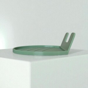 May include: A sage green, minimalist tray with a raised, U-shaped handle. The circular tray has a series of parallel grooves. The design is simple and modern, suitable for various uses.