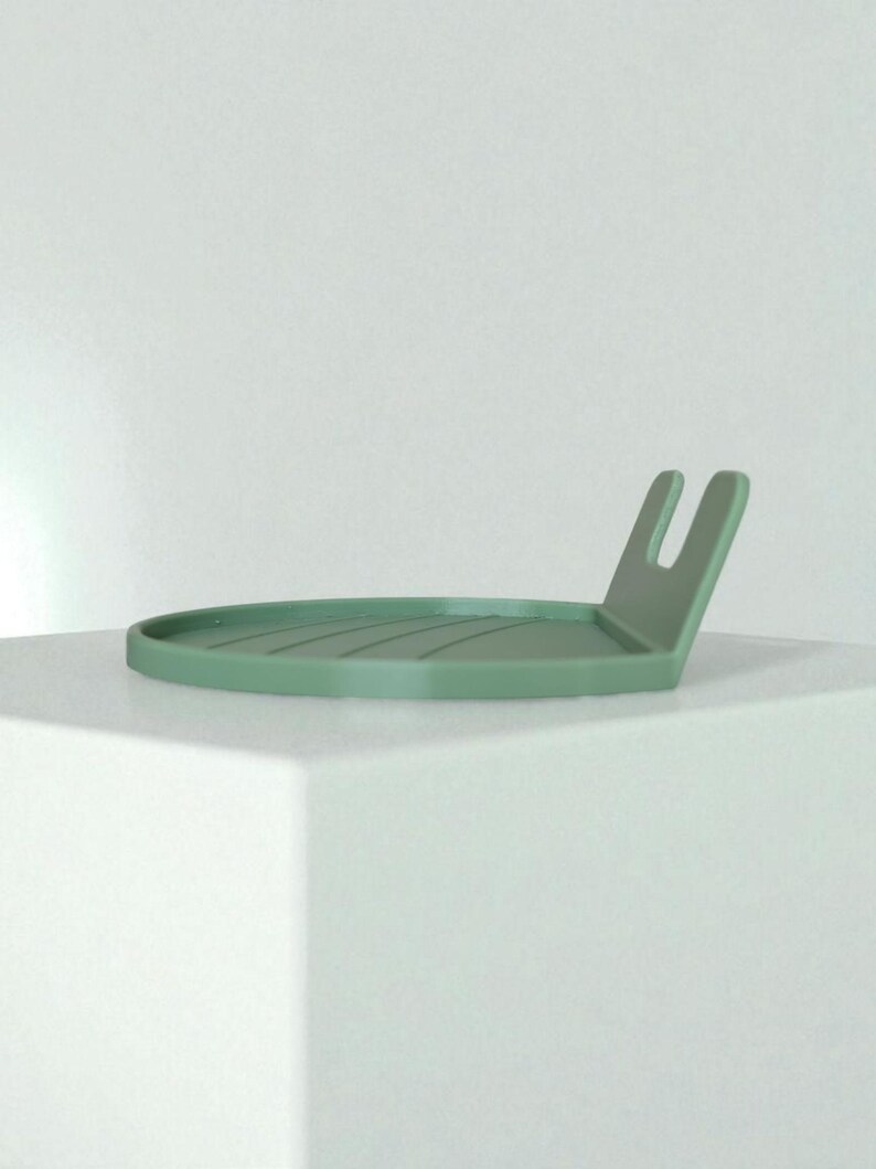 May include: A sage green, minimalist tray with a raised, U-shaped handle. The circular tray has a series of parallel grooves. The design is simple and modern, suitable for various uses.