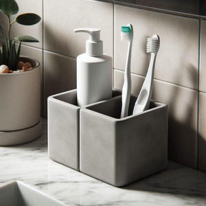 May include: A gray concrete bathroom organizer with two compartments. One compartment holds a white soap dispenser, and the other holds two white toothbrushes with green and white bristles. The organizer sits on a marble surface.