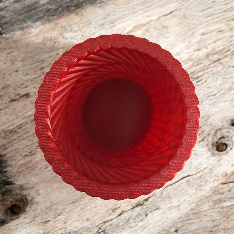 May include: A top-down view of a red, textured vase. The vase has a spiral design on the inside and a scalloped edge. The vase is made of a solid red material.