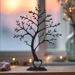 May include: A black metal tree-shaped jewelry holder with a heart-shaped base. The tree has many branches for hanging necklaces and earrings. The background shows a window with a sunset and a vase with decorative lights.