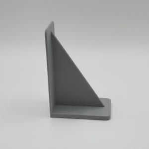 Op de afbeelding: Een grijze, L-vormige boekensteun met een driehoekige steun. De boekensteun is gemaakt van een solide materiaal en heeft een gladde, matte afwerking. De basis is rechthoekig en de steun is schuin.