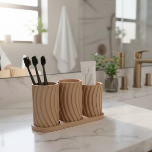 May include: A wooden bathroom organizer with three cylindrical holders. The holders have a ridged design and are arranged on a rectangular base. Three black toothbrushes and a tube of toothpaste are visible.