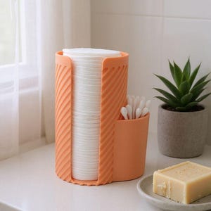 May include: An orange cosmetic organizer holds a stack of white cotton pads and a small container of cotton swabs. A small potted succulent and a bar of soap on a dish are also visible.