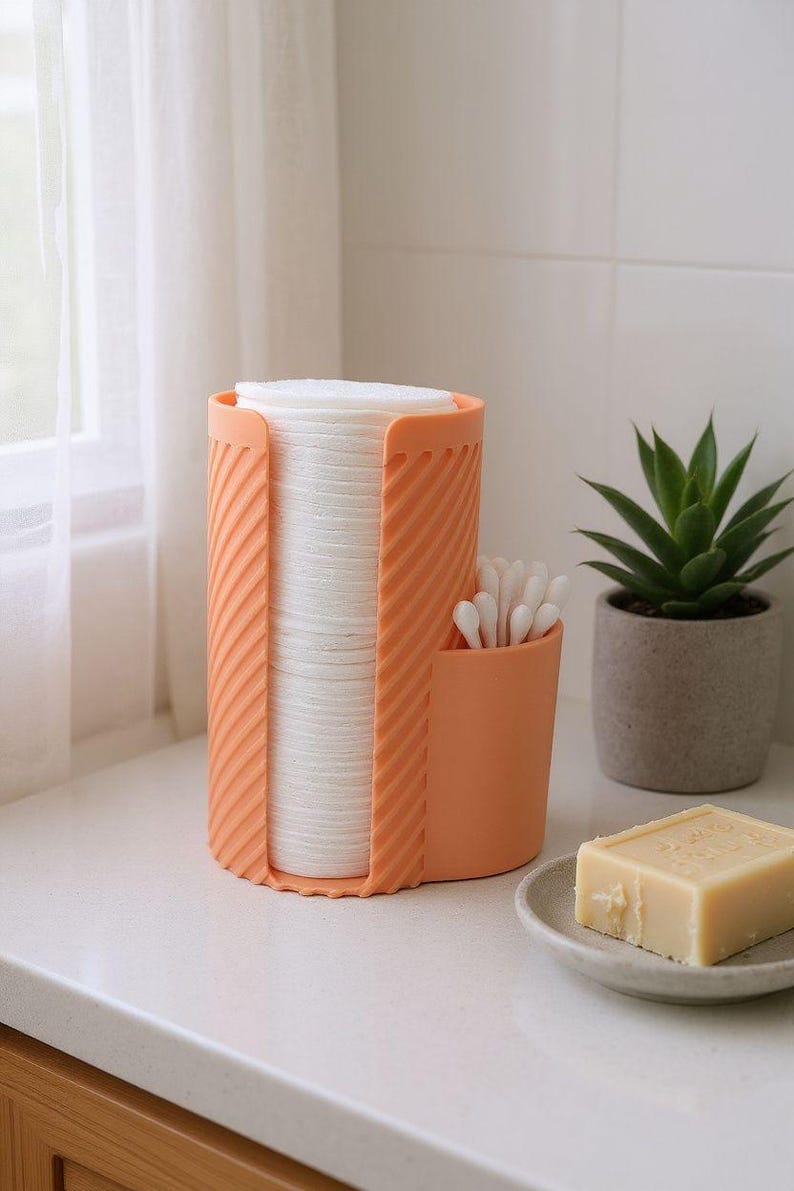 May include: An orange cosmetic organizer holds a stack of white cotton pads and a small container of cotton swabs. A small potted succulent and a bar of soap on a dish are also visible.
