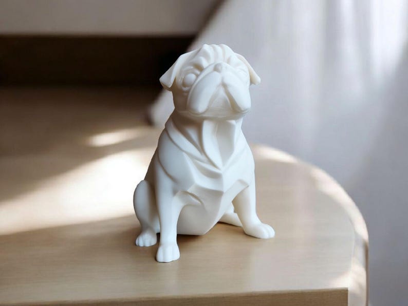 K&ouml;nnte beinhalten: Eine wei&szlig;e Keramikfigur eines Mops-Hundes in sitzender Position. Der Mops hat ein detailliertes, geometrisches Design mit sichtbaren Falten und Knicken. Die Figur steht auf einer hellen Holzoberfl&auml;che.